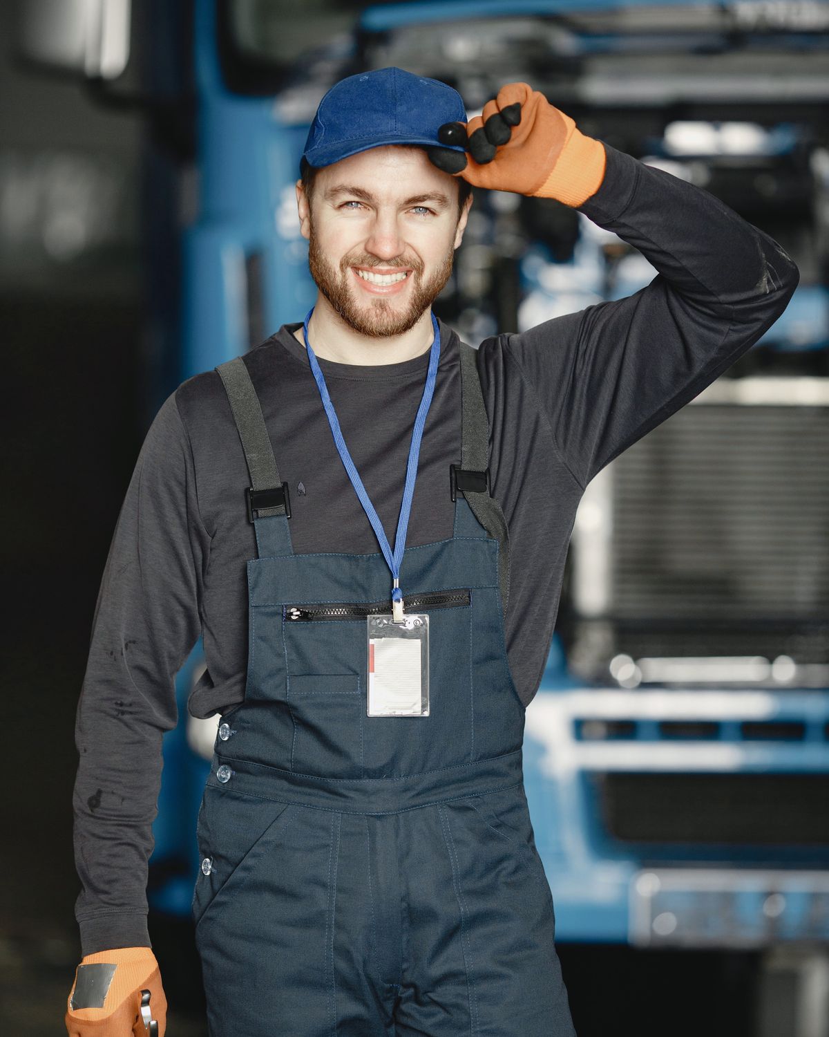 Smiling diesel mechanic in work overalls and gloves standing in front of a truck